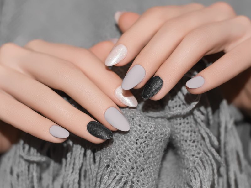 Female hands with gray nail design. Glitter black nail polish manicure. Woman hands on gray wool background.